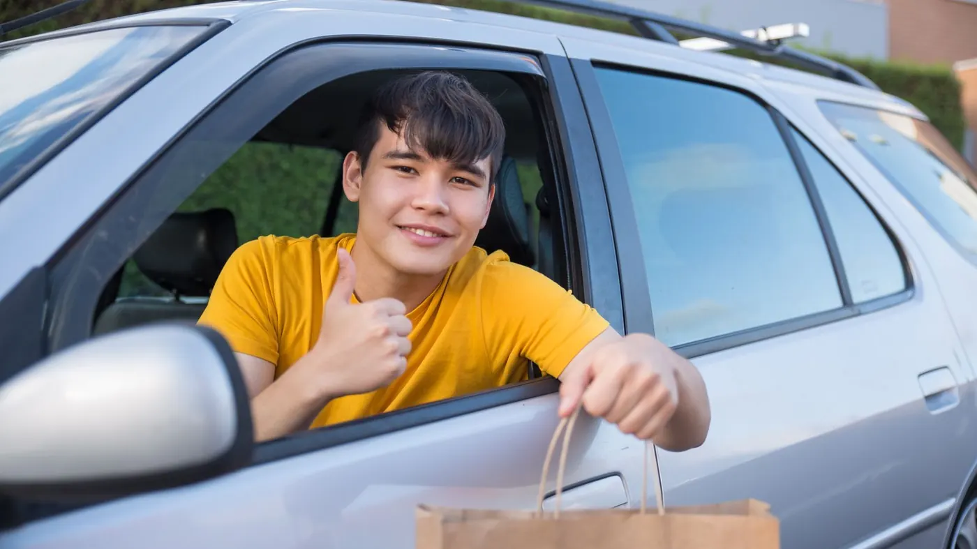 Delivery driver handing a takeout bag from his car